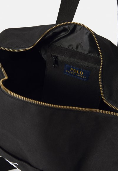 Crna torba sa zlatnim patentnim zatvaračem, koja ima prostrano unutrašnjost, mali džep sa patent zatvaračem i plavu oznaku Polo Ralph Lauren unutra.