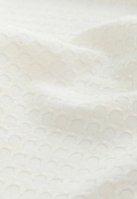 White textured fabric featuring a geometric pattern of raised circles, soft quality, and a slightly undulating surface.