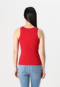 Rød ribbet tanktop med en tætsiddende design og brede stropper, parret med lyseblå jeans med en klassisk baglomme design.