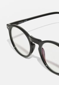 Gafas de sol de montura redonda en plástico negro con lentes transparentes. Las características incluyen una forma de puente distintiva y una marca en el interior de la patilla.