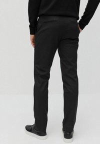 Zwarte op maat gemaakte broeken van een gladde stof, met een rechte snit en een vlakke tailleband. Twee achterzakken en subtiele stiksels.