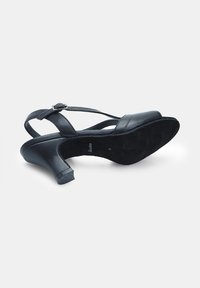 Sandal nero con tacco alto, con tomaia in pelle liscia, design a fasce incrociate e suola in suede testurizzato. Presenta una fibbia per una calzata sicura.