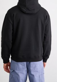 Felpa nera con cappuccio dalla vestibilità comoda, caratterizzata da orlo e polsini a coste. Indossata con pantaloni cargo azzurri chiaro con tasche laterali.