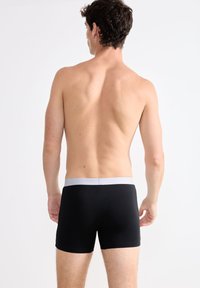 Boxer neri con un morbido elastico grigio, vestibilità aderente, tessuto liscio e un design semplice, visti da dietro su un torso nudo.