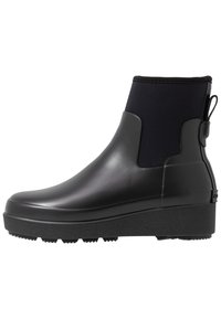 Botte de pluie noire au niveau de la cheville, dotée d'un corps en caoutchouc lisse, d'un haut en textile élastique, d'une languette et d'une semelle plateforme texturée pour une meilleure adhérence.