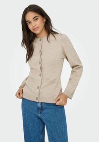 Cardigan beige en matériau doux, avec un devant boutonn�é, un col rond, des poignets côtelés et deux poches avant.