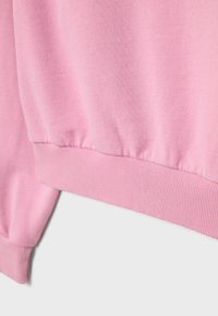 Nahaufnahme von rosa Sweatshirtstoff, der gerippte Bündchen- und Saumdetails vor einem einfarbigen Hintergrund zeigt.