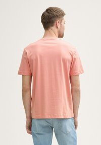 Camiseta de algodón de manga corta y cuello redondo en rosa claro, con costuras visibles, textura suave, combinada con jeans de mezclilla azul claro, vista de perfil lateral.
