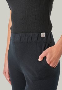 Schwarze gerippte Strickhose mit elastischem Bund, Seitentasche und kleinem Logotag. Der Stoff hat eine weiche Textur und eine figurbetonte Form.