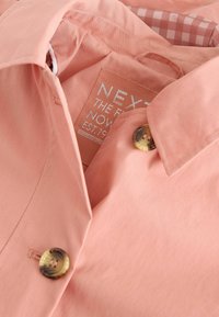 Light pink shirt featuring a collar, round buttons, and a woven label inside. The interior has a checked pattern in contrasting colors.