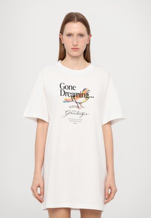 T-shirt blanc oversize à manches courtes, avec un graphisme d'oiseau coloré et un texte noir disant "Parti rêver..." et "Salutations".