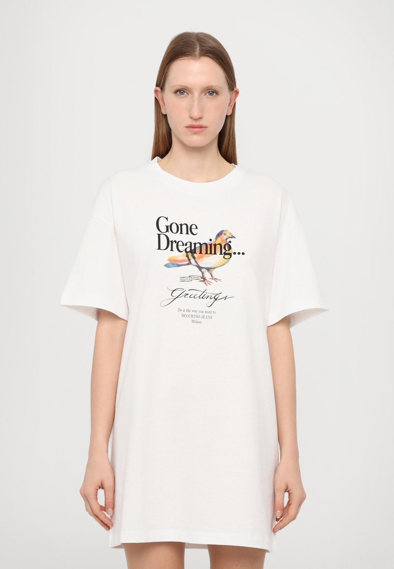Balta didelė t-shirt su trumpomis rankovėmis, su spalvingo paukščio iliustracija ir juodu tekstu „Nuskridau svajoti...“ ir „Sveikinimai“.
