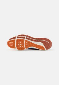 Semelle de chaussure avec un motif complexe. Comprend un mélange de caoutchouc orange et rouge, segmenté pour l'adhérence, et une semelle intermédiaire blanche et lisse.