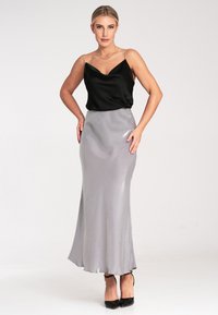 Schwarzes Satin-Top mit feinen Trägern, kombiniert mit einem silbernen Satinkleid, das eine ausgestellte Form und eine glatte Textur aufweist, getragen mit schwarzen High Heels.