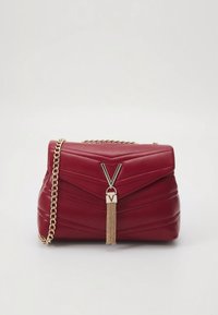 Röd quiltad läderhandväska med guldkedjestrap och guldfärgad "V"-logokloss med kedjetofs på en enkel ljus bakgrund.