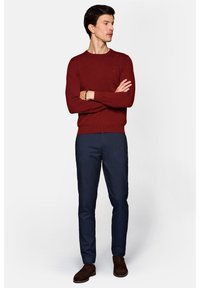 Czerwony sweter dzianinowy z okrągłym dekoltem i prążkowanym wykończeniem. Połączony z ciemnoniebieskimi spodniami o dopasowanym kroju i brązowymi zamszowymi butami.