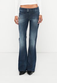 Széles szárú sötétkék farmernadr�ág denimből, középmagas derékkal, két első zsebbel és finom kifakítással. Fekete hegyes orrú cipővel párosítva.