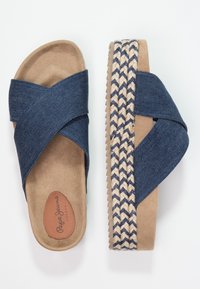 Ett par beige plattformssandaler med blå denimkorsband och vävda jute-detaljer på sulans kant, med synlig logotyp på innersulan.