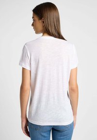 Camiseta blanca de manga corta con cuello redondo y un corte holgado, que presenta una textura sutil y un dobladillo recto.