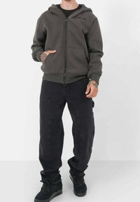 Mörkgrå zip-up hoodie med framficka och huva, kombinerad med svarta cargobyxor. Outfiten har en avslappnad passform och texturerad tyg.