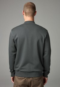 Tamno siva dukserica s okruglim izrezom, rebrastim manžetama i donjim rubom. Glatka tekstura, opušteni kroj i minimalistički dizajn bez vidljivih logotipa ili uzoraka.
