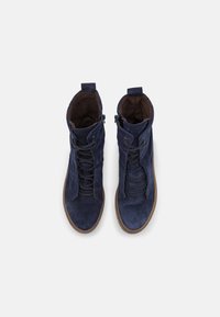 Bottines en suède bleu marine avec un laçage à l'avant, une fermeture éclair et une surface texturée. Semelle en caoutchouc marron et doublure intérieure douce.