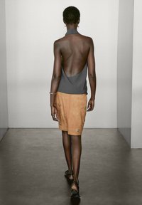 Haut dos nu gris à bretelles, associé à une jupe en daim tan ornée de motifs d'étoiles brodés. Le modèle porte des sandales noires, vu de dos.