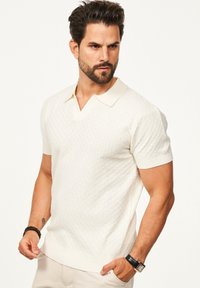 Kurzärmliges, cremefarbenes Poloshirt mit strukturiertem Strickmuster, klassischem Kragen und gerippten Bündchen und Saum.