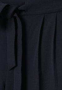 Tissu plissé bleu marine avec un détail de taille attachée, présentant une texture lisse et un design structuré.