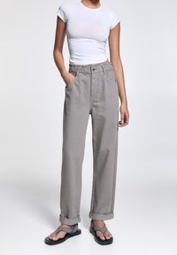 Pantalon gris ample avec une taille élastique, comportant deux poches latérales, des manches retroussées, et associé à des sandales grises.