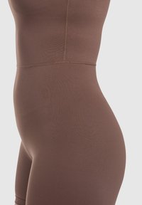 Brun sömlös bodysuit med en slät textur, figurnära design och diskreta sömnadsdetaljer längs midjan och sidorna.