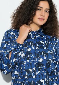 Blauw overhemd met knopen, met een abstract patroon in donkerblauw, wit en lichtblauw. Lange mouwen met een losse pasvorm en een kraag.