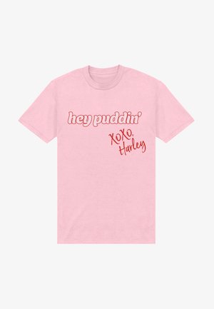 T-shirt rose clair avec texte rouge « hey puddin' » en gras et « XOXO, Harley » en style manuscrit sur le devant.