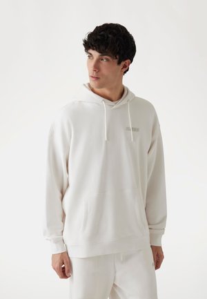 White hooded sweatshirt with a front pocket and drawstring. Features a subtle logo on the chest. Fabric has a soft, smooth texture.
