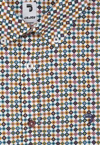 Multikleurige geborduurde overhemd met een geometrisch design, voornamelijk in blauw, geel, roze en zwart, met witte stof en contrasterende knopen.