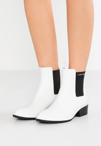 Botas Chelsea blancas con paneles laterales elásticos negros, de un material sintético suave, puntera afilada y tacón bajo de bloque.