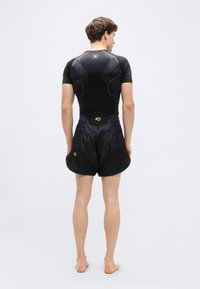 Μαύρο αθλητικό μπλουζάκι με υφή σχεδίου και μαύρο σορτς με κοντό μήκος, με στιλιζαρισμένη μέση και διακριτικό σχέδιο, ορατά από πίσω.