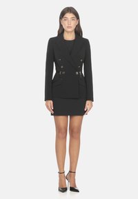 Blazer nero su misura con bottoni dorati doppi, dotato di tasche laterali e una mini gonna aderente. Completato con tacchi in vernice.