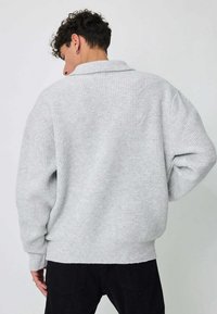 Pull gris en tricot, coupe ample, manches larges et col. Présente un motif texturé ainsi qu'un ourlet et des poignets côtelés. Vue de dos.