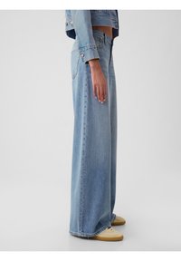 Jasnoniebieskie szerokie dżinsy wykonane z denimu, z wysokim stanem, surowymi brzegami i luźnym krojem. Połączone z jasnymi butami.
