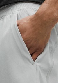 Šviesiai pilki sportiniai šortai su elastinga juosmena ir šonine kišenė. Minkšta medžiaga su lygiu paviršiumi ir tvarkingais siūlėmis.