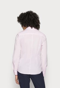 Camicia a maniche lunghe rosa chiaro con vestibilità adattata, chiusura con bottoni davanti, orlo curvo e colletto. Tessuto liscio con leggera lucentezza e bottoni ai polsini.