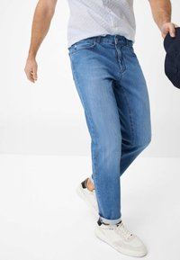 Jeans in denim azzurro chiaro con un taglio dritto, caratterizzati da un design a cinque tasche e dettagli di cucitura sottili. Indossati con sneakers bianche.