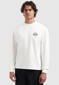 Weißes Langarmshirt aus Baumwolle mit Rundhalsausschnitt und kleinem grafischen Logo auf der linken Brust. Geschmeidige Textur, lässige Passform.