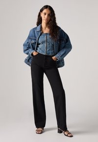 Spijkerjas met een losse pasvorm over een cropped spijkerbloes, in combinatie met een zwarte hoge taille wijde broek en zwarte bandenhakken.