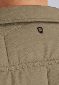 Camisa de tela de pana color caqui con un diseño de acolchado cosido y una etiqueta negra de marca con "PME Legend" en la parte posterior del escote.