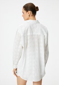 Camisa blanca de manga larga con un patrón texturizado de hojas, corte relajado y cuello con solapa. Tejido suave y dobladillo redondeado.