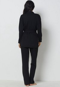 Set lounge nero composto da un top a maniche lunghe con vita cinturata e pantaloni dritti, entrambi in un tessuto liscio e morbido.