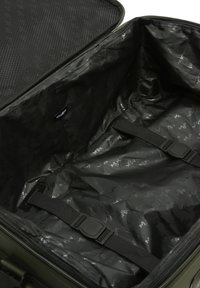 Interno di una valigia verde con un rivestimento nero testurizzato e un motivo con logo, cinghie regolabili per fissare il contenuto e chiusura con zip.