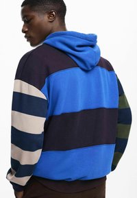 Hooded sweatshirt with multicolored horizontal stripes in blue, navy, beige, and green; made of soft cotton blend fabric.